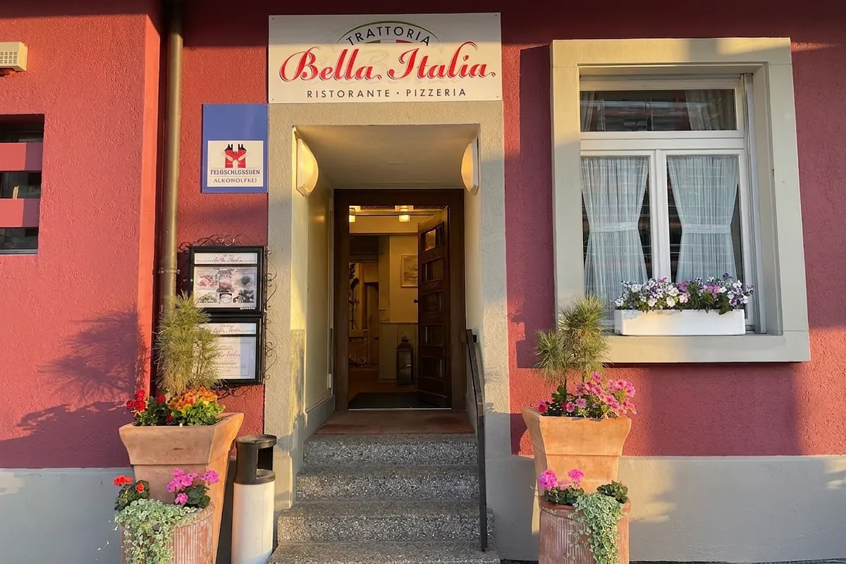 Eingang der Trattoria Bella Italia an der Freiburgstrasse mit Schriftzug über der Tür, Blumenkästen und Aushang, in warmem Nachmittagslicht.